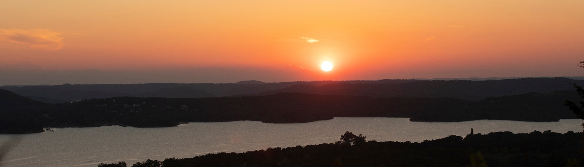 Panorama of a fiery orange sunset behind the Branson hills with Table Rock Lake in the foreground.