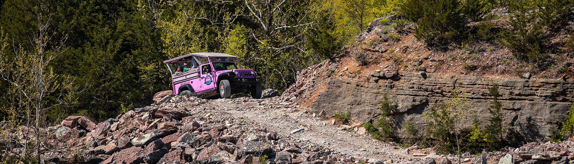 Header image of a Pink Jeep Wrangler approaching the top of a rocky 4x4 trail with trees in background, Branson, Missouri.