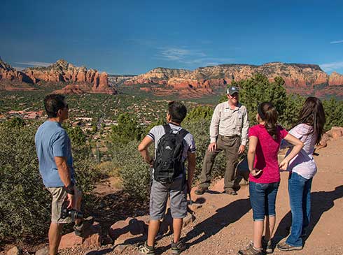 Pink Adventure Tour guide and Scenic Sedona tour guests at Airport Mesa Overlook with West Sedona's red rock landscape in the background.