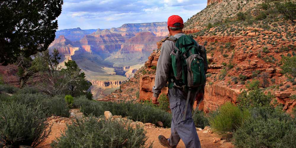 Rear view of hiker with backpack as he walks on a dirt trail toward a view of the Grand Canyon South Rim.