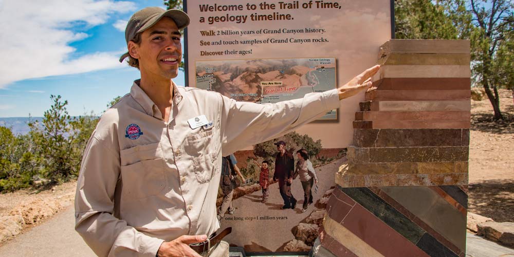 Pink Adventure Tour guide interpreting the geology timeline display at the Grand Canyon's Trail of Time entrance.