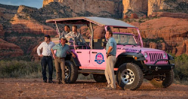 Peoplebyjeep Discoverwonder 380X200 Tour guide and guests beside a Pink Jeep Wrangler, looking golden sunlight falling on red rocks in background.