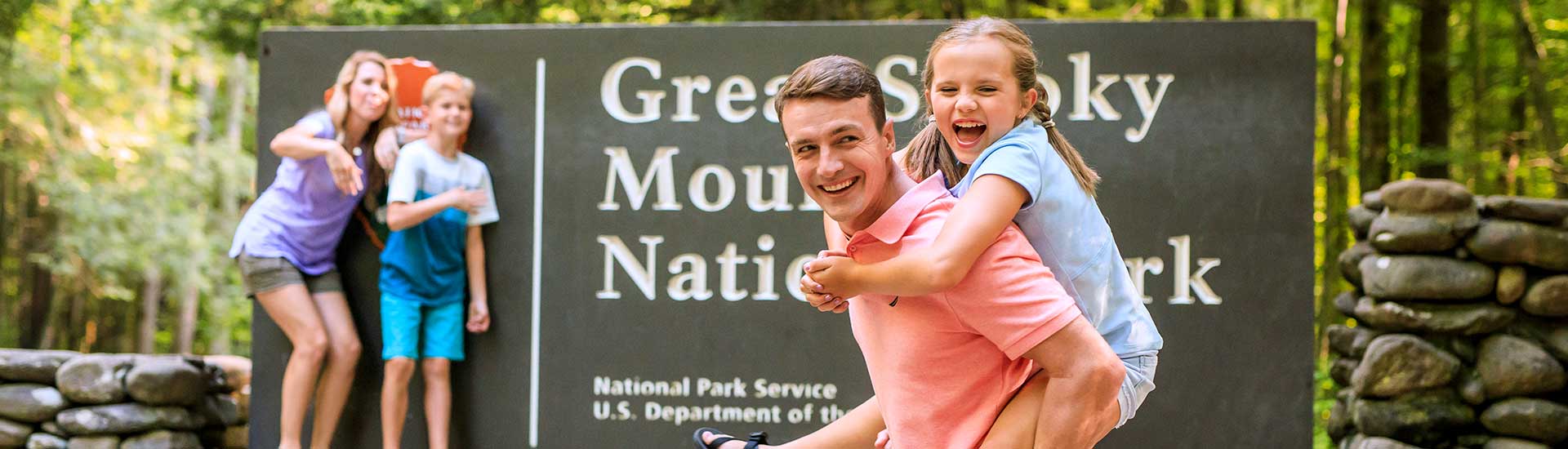 Family of four laughing and posing in front of the Great Smoky Mountains National Park sign during a Smoky Mountains Pink Jeep Tour, Gatlinburg, TN.