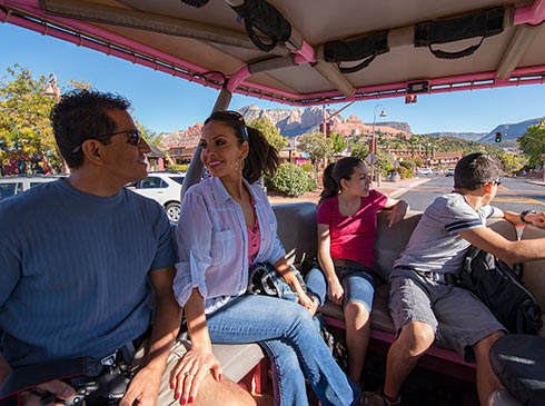 Family of four seated in the back of an open-air Pink Jeep Wangler with view  Uptown Sedona in the background.