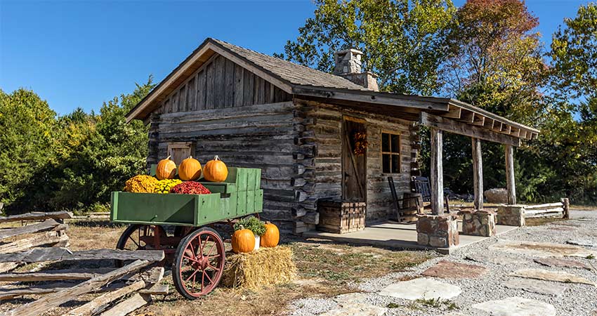 A historic hand-hewn log cabin sits atop Baird Mountain with pumpkin wagon in foreground, tour with Pink Jeep Tours Branson.