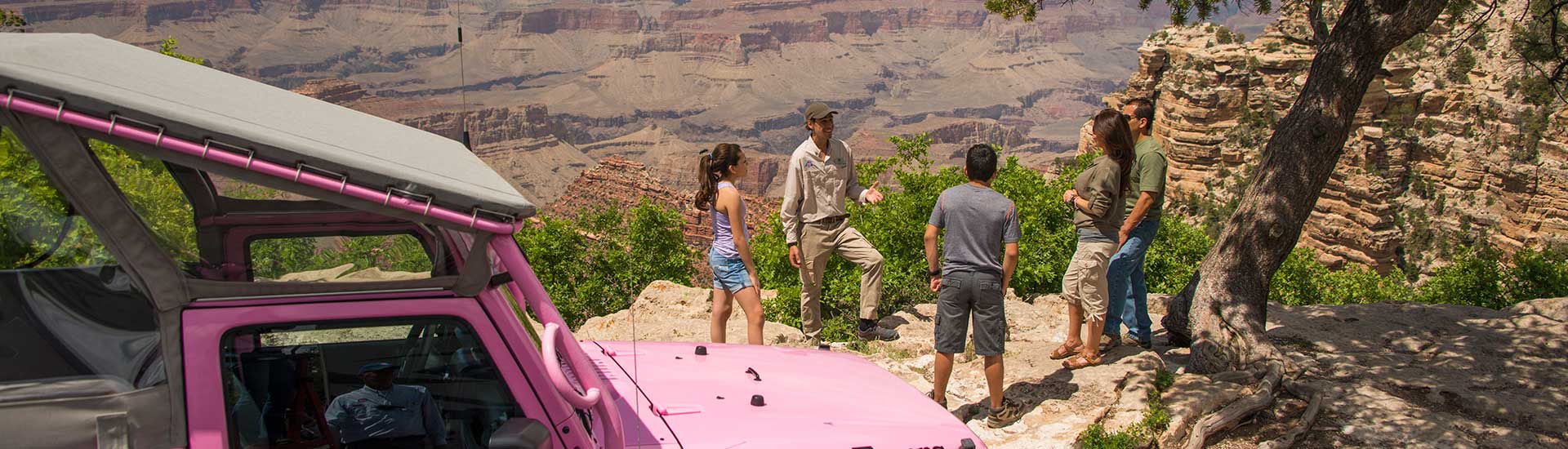 Desert View Sunset tour guests with guide overlooking the Grand Canyon's South Rim with Jeep® Wrangler in foreground.