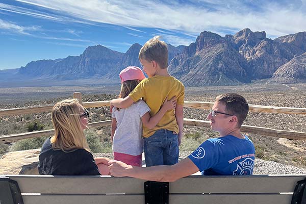 Parents and two young kids are seated on a bench facing a beautiful panorama of Red Rock Canyon National Conservation Area, near Las Vegas, Nevada.