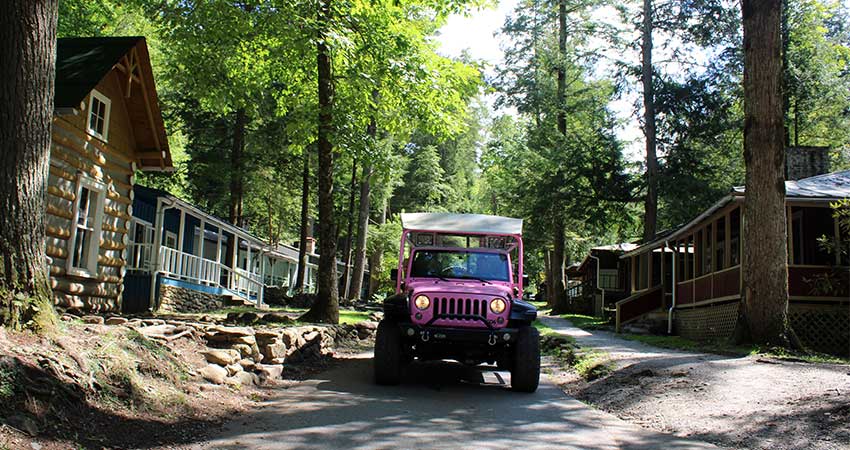 Pink Jeep Wrangler driving past restored cabins at Daisy Town, Elkmont Ghost Town, Great Smoky Mountains National Park.