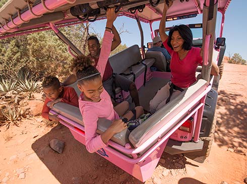 Family laughing and holding onto the rails in a Pink Jeep Wrangler while climbing a steep incline on the Broken Arrow Trail, Sedona, AZ. 