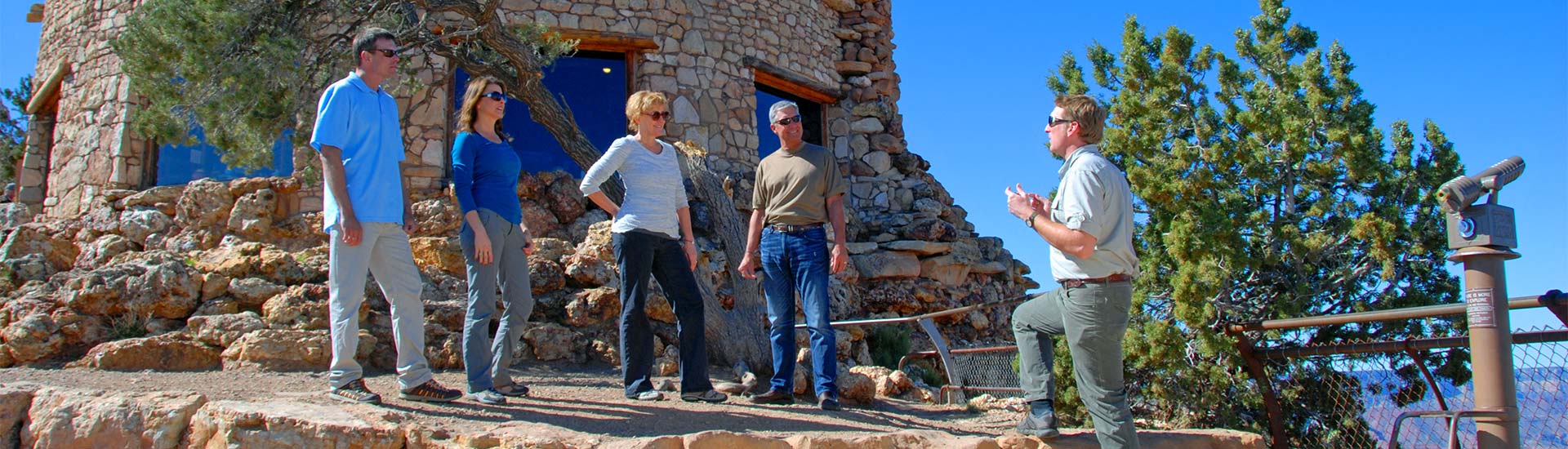 Pink Jeep Tour guide talking with guests while standing on a terrace in front of the Desert View Watchtower, along 