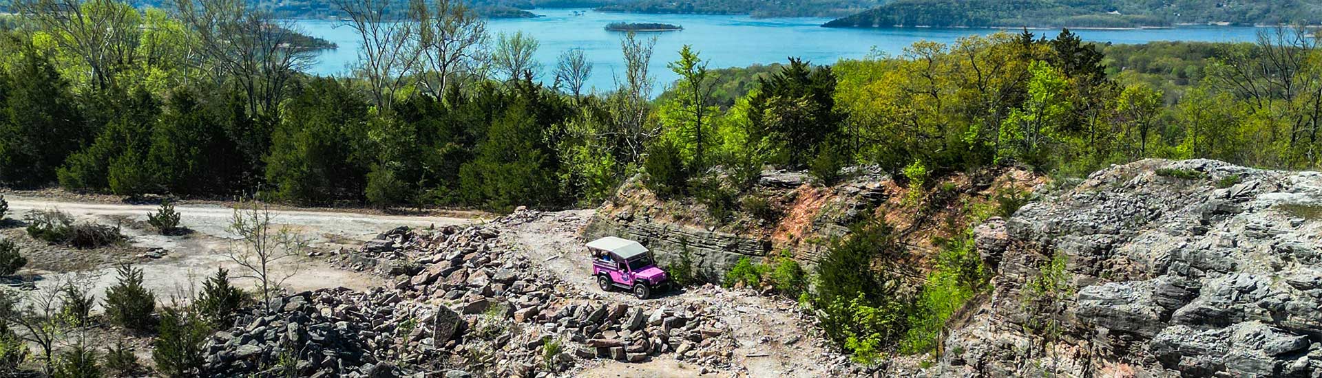 Aerial view of Pink Jeep Wrangler navigating a rocky off-road trail below Baird Mountain, with Table Rock Lake in the distance, Branson, MO.