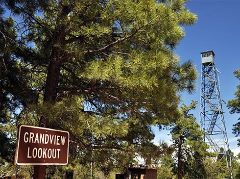 Grandview Lookout sign with ponderosa pine trees and lookout tower in the background against a blue sky, Kaibab National Forest, Northern AZ.