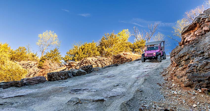 Pink Jeep Wrangler descending a steep rocky trail with autumn foliage from atop Baird Mountain in the Ozarks, near Branson, MO.