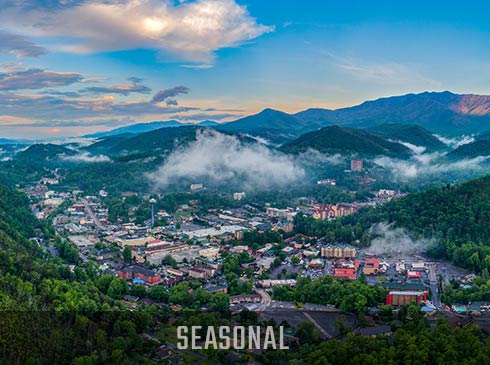 Aerial view of Downtown Gatlinburg against a blue sky filled with clouds, with Seasonal banner.