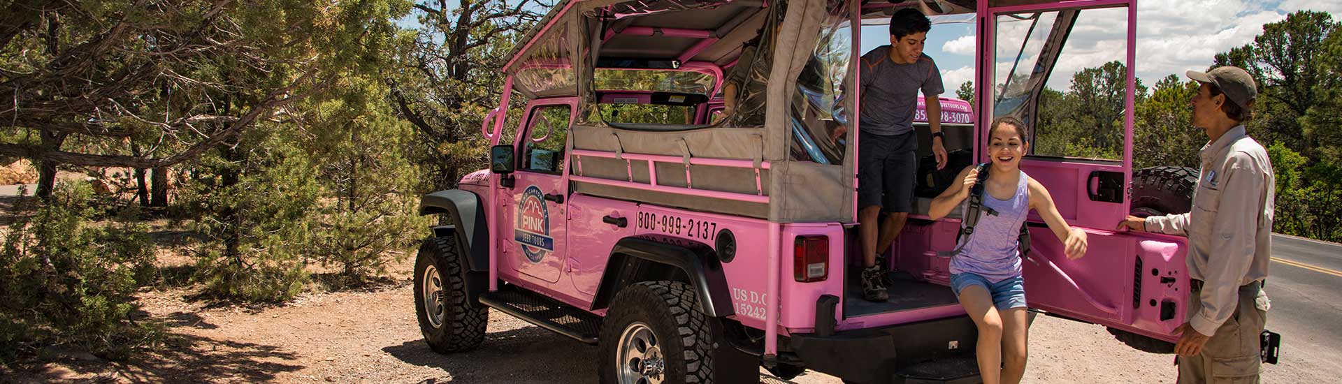 Teenage girl and boy exit the back of a Pink Jeep Wrangler parked along the South Rim, aided by a Pink Jeep Tours Grand Canyon adventure guide.