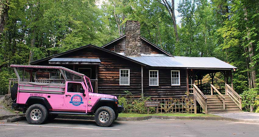 Smoky Mountains Pink Jeep Tour's Jeep Wrangler parked in front of the historic Appalachian Club surrounded by thick green forest.