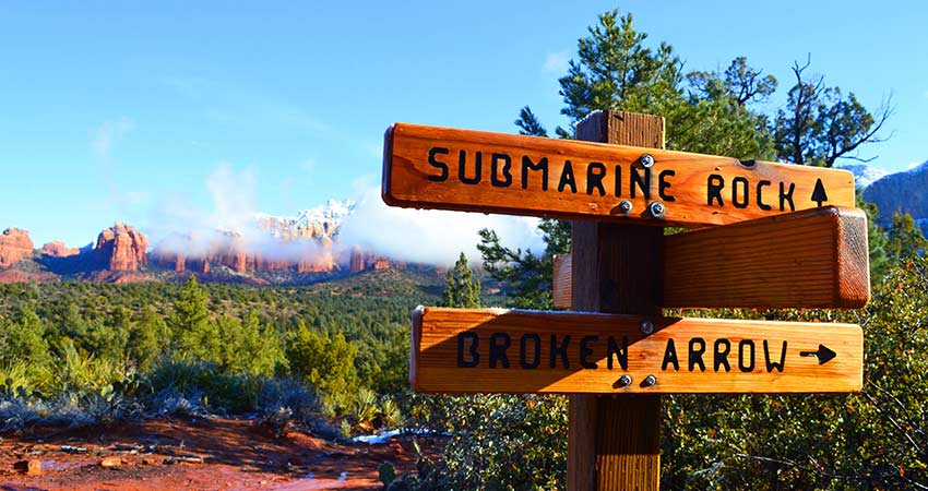 Signage at the junction of Submarine Rock and Broken Arrow trailheads with Sedona red rocks in background, lightly dusted with snow.