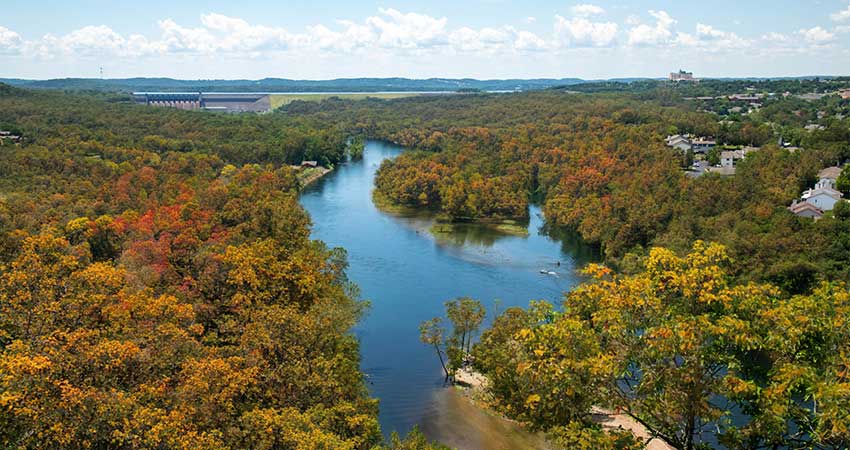 Overlook of Lake Taneycomo surrounded by fall foliage with Table Rock Dam in the distance, seen from the Branson Scenic Overlook.