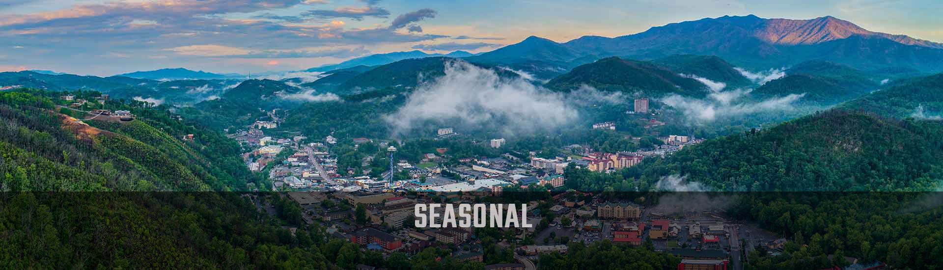 Aerial view of the Smoky Mountains foothills surrounding Downtown Gatlinburg against a blue sky with hovering clouds.