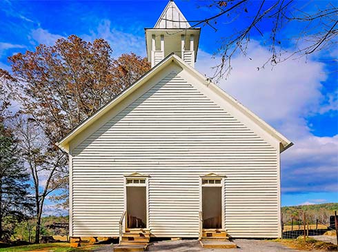 The Cades Cove Methodist Church, built in 1902, is surrounded by a brilliant blue sky an rust autumn trees in Cades Cove, TN.