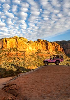 Sedona's red rock with the golden glow of late afternoon light and a Pink Jeep Wrangler perched atop a slickrock on the Broken Arrow Trail.