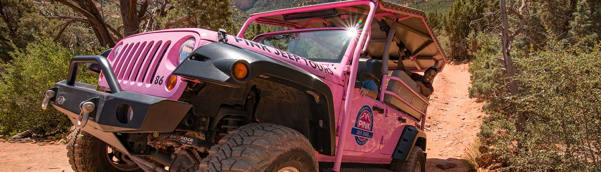 Closeup of a Pink Jeep Wrangler climbing up a steep incline on the Broken Arrow Trail, with a sunburst on its windshield, 