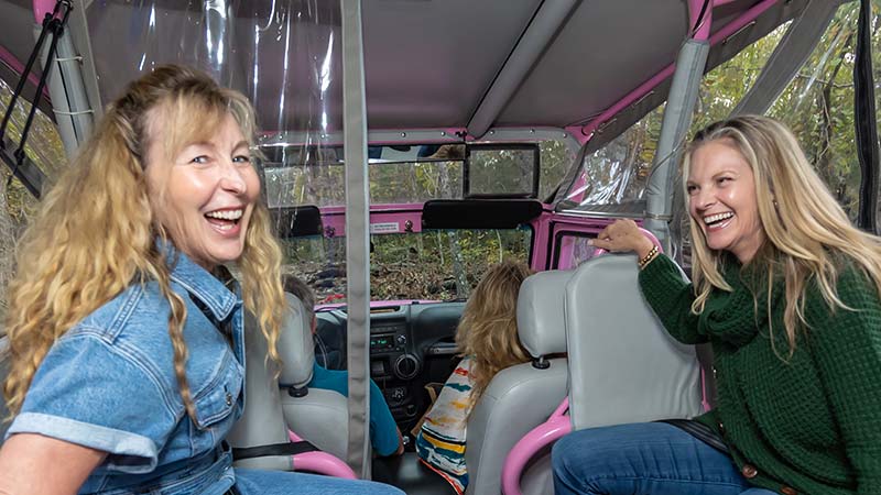 Two ladies laughing at the camera from inisde the back of a Pink Jeep Wrangler during an Ozark Mountain Crawl Tour, Branson, MO.