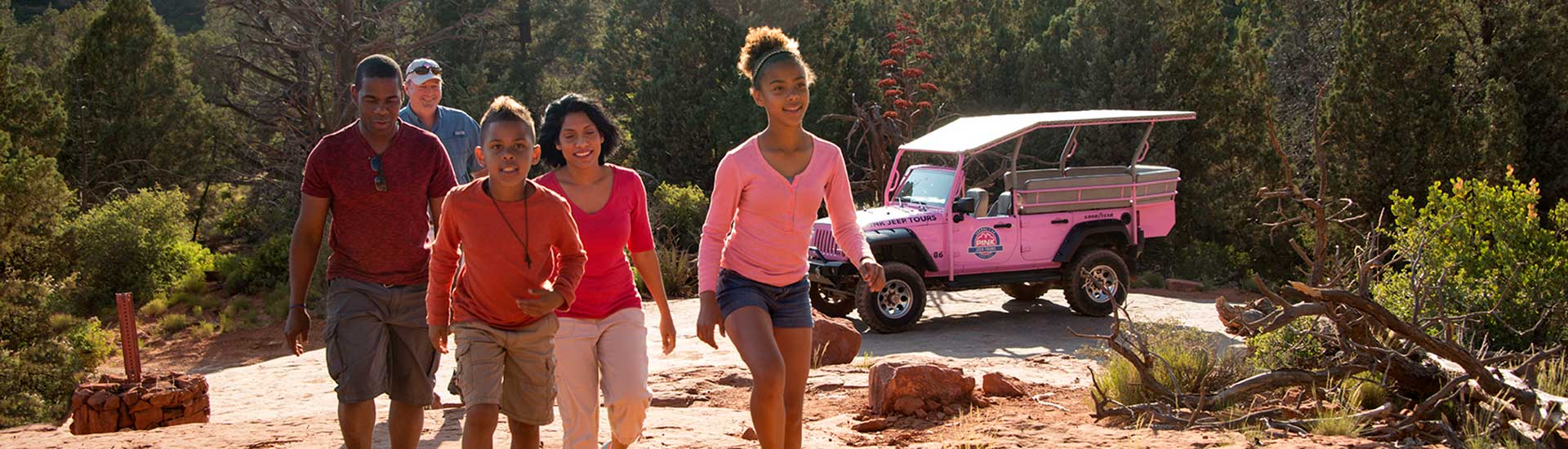 Family walking up a trail towards the camera with a Pink Jeep Wrangler parked in the background, Pink Jeep Tours Broken Arrow Twilight tour.