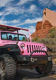 Closeup of the front of a Pink Jeep Wrangler as it drives past the Chapel of the Holy Cross in Sedona, AZ. Pink Jeep Scenic Sedona tour.