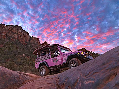 Pink Jeep Wrangler with tour guests sits atop Sedona's slickrock under a pink, purple sky during the Broken Arrow Twilight tour.