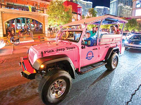 Pink Jeep Las Vegas adventure guide driving a Pink Jeep Wrangler with tour guests down the Las Vegas Strip at night on the Bright Lights tour.