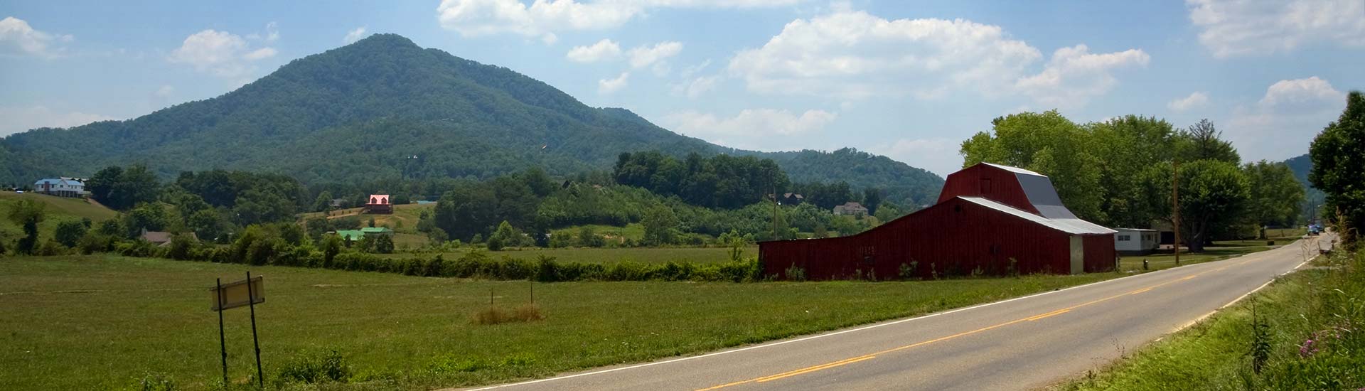 Scenic farm landscape with red barn along Wears Valley Road with the blue ridges of the Smoky Mountains foothills in the distance.