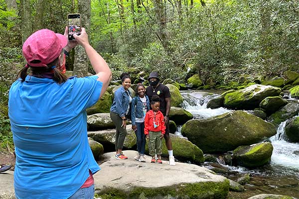 Smoky Mountains Pink Jeep adventure guide taking a photo of a family posing on a rock in the Roaring Fork Stream, along the Roaring Fork Motor Nature Trail.