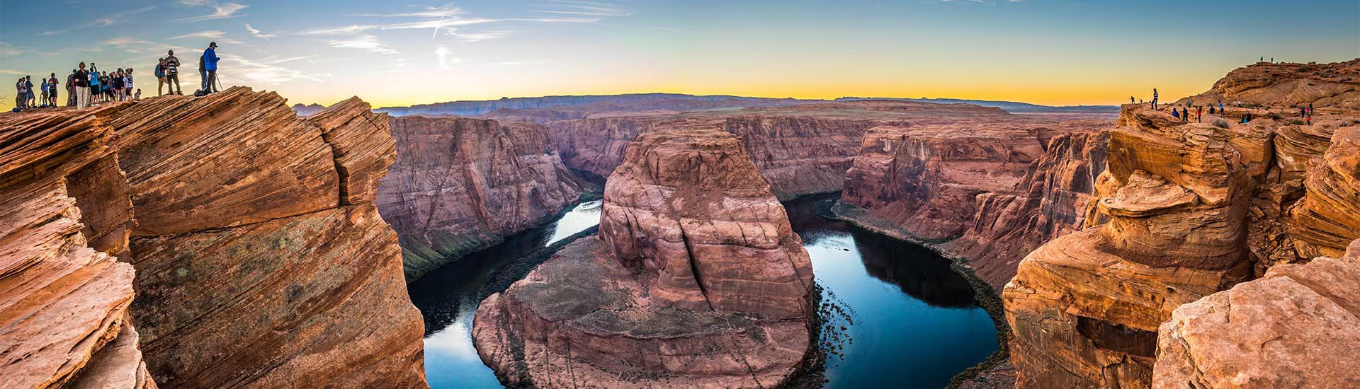 Visitors at the edge of the Grand Canyon rim, overlooking Horseshoe Bend and Colorado River during sunset.