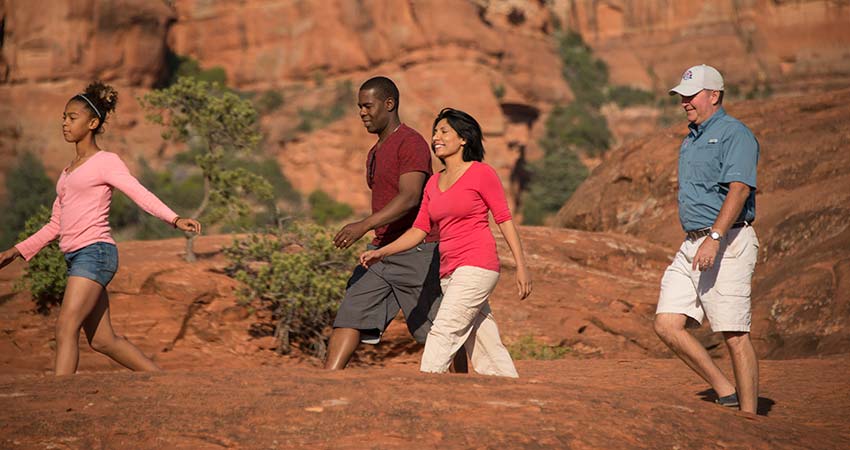 Pink Adventure Tour guide and three guests walking across the sandstone slickrock at Submarine Rock while on Sedona's signature Broken Arrow tour.