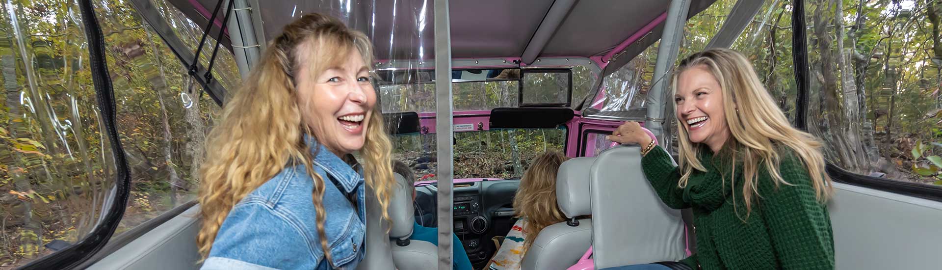 Two ladies laughing at the camera while seated in the back of a Pink Jeep Wrangler on an off-road trail up Baird Mountain, Branson, MO.