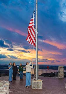 Pink Jeep tour guide and guests retreating the American flag atop Baird Mountain during a twilight sunset, Branson, MO.