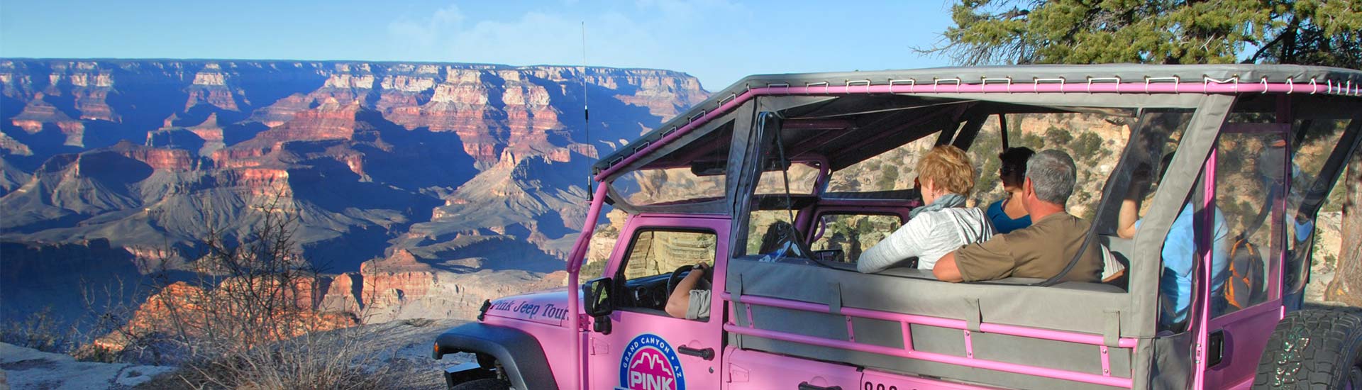 Guests sitting in an open-air Jeep Wrangler facing a dramatic view of the  Grand Canyon's South Rim, on Pink Jeep Tours Grand Canyon's Desert View Off-road Tour.