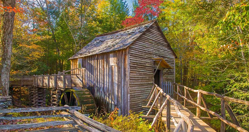 Autumn foliage envelops the Cable Grist Mill, water wheel and split rail fence, in the Cable Mill Area of Great Smoky Mountains National Park.