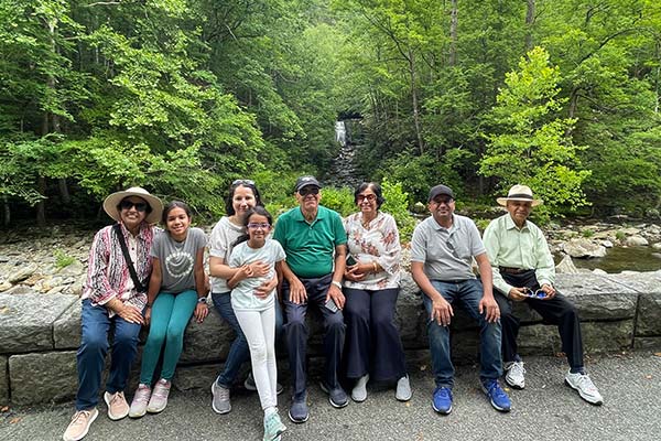 Multigeneratonal Indian family of eight people seated on a stone wall in front of the Roaring Fork stream amidst a lush forest in the Smoky Mountains, TN.