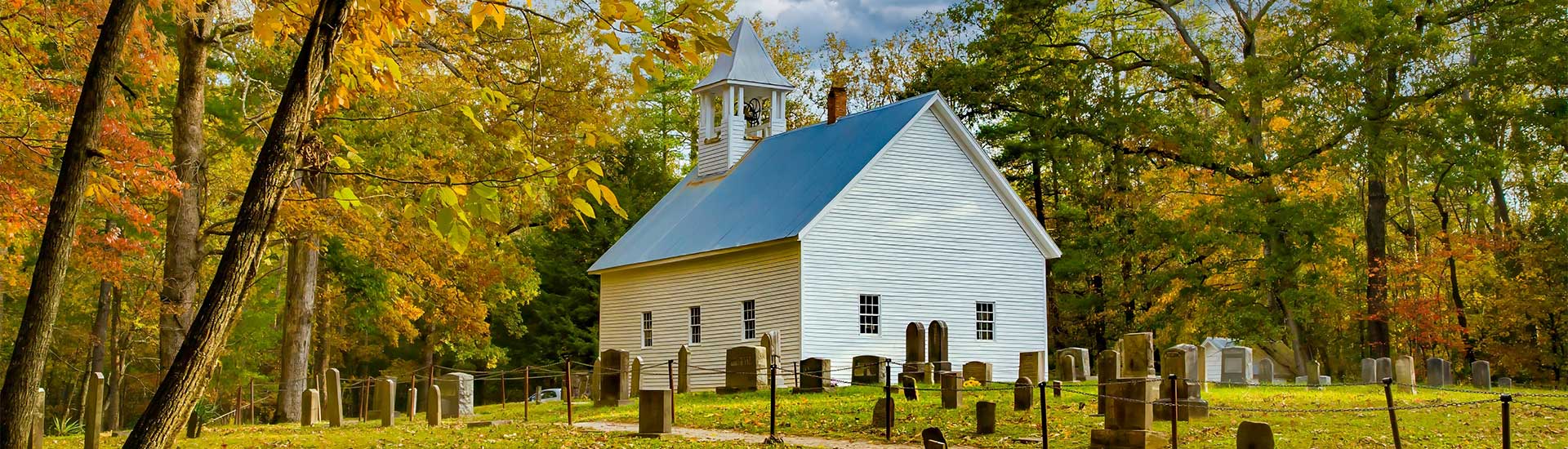 Autumn trees surround the restored Cades Cove Primitive Baptist Church and graveyard, located in Great Smoky Mountains, Tennessee.