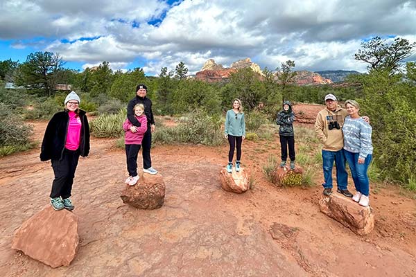 Multigenerational family members standing on individual boulders with beautiful Sedona landscape in the background, Pink Jeep Tours’ Coyote Canyon Tour.