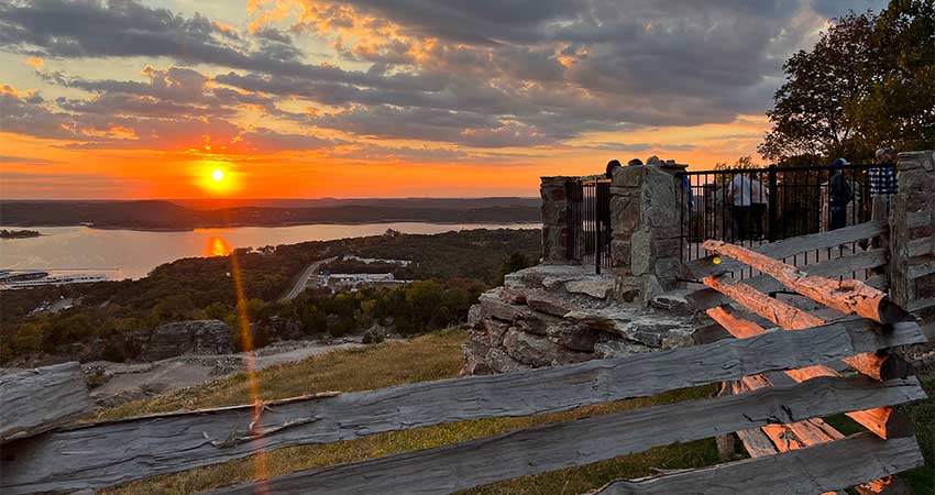 Scene of a golden-orange sunset over Table Rock Lake with a split rail fence in the foreground, Pink Jeep Tours exclusive Baird Mountain overlook. 