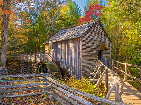 Historic water wheel and grist mill with a split rail fence surrounded by vibrant autumn trees, Cades Cove Scenic Loop, Smoky Mountains, TN.